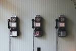A group of three vintage telephones lined up against a wall.